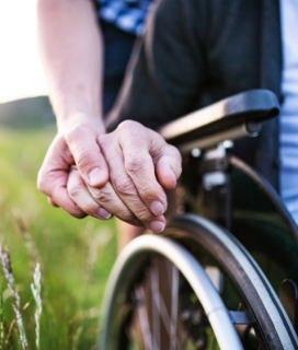 Close-up of a nurse holding a man's hand in a wheelchair, representing the care and support ALS patients need. Awareness post by Southwest Urgent Care Telfair - Sugar Land on ALS with FAQs and details.
